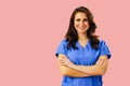 Portrait of smiling female doctor or nurse in blue uniform with arms crossed on pink studio background Royalty Free Stock Photo