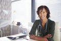 Portrait Of Smiling Female Doctor With Stethoscope Sitting Behind Desk In Office