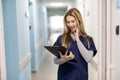 Portrait Of Smiling Female Doctor Wearing Scrubs Standing In Hospital Corridor Holding Clipboard Royalty Free Stock Photo