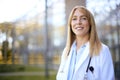 Portrait Of Smiling Female Doctor Wearing White Coat Standing Outside Modern Hospital Building Royalty Free Stock Photo
