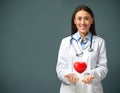 Portrait of smiling female doctor wearing white coat and stethoscope with a heart levitating above her hands and copy space