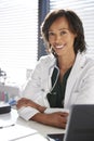 Portrait Of Smiling Female Doctor Wearing White Coat With Stethoscope Sitting Behind Desk In Office Royalty Free Stock Photo