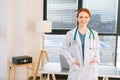 Portrait of smiling female doctor in white coat standing on background of window in sunny day in light medical clinic Royalty Free Stock Photo