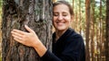 Portrait of smiling female ecology activist hugging big old tree in forest. Concept of ecology, environment protection