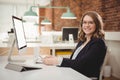 Portrait of smiling female executive using mobile phone while working on computer Royalty Free Stock Photo