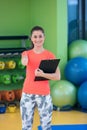 Portrait of smiling female fitness instructor writing in clipboard while standing in gym Royalty Free Stock Photo