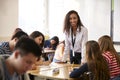 Portrait Of Smiling Female High School Teacher Standing By Student Table Teaching Lesson