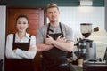 Portrait of  smiling female and male barista wearing apron, standing with crossed arms at coffee shop counter bar, waitress and Royalty Free Stock Photo