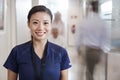 Portrait Of Smiling Female Nurse Wearing Scrubs In Busy Hospital Corridor Royalty Free Stock Photo