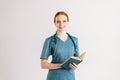 Portrait of smiling female physician in green uniform with stethoscope holding medical book standing and looking at Royalty Free Stock Photo