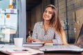 Portrait of smiling female student writing looking at camera sitting at table