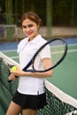 Portrait of smiling female tennis player with racket and ball standing by net at the outdoor tennis court Royalty Free Stock Photo