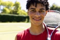 Portrait of smiling fit biracial man with tennis racket on sunny outdoor tennis court, copy space Royalty Free Stock Photo