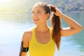 Portrait of a smiling fitness girl with arm band fixing her hair while standing outdoors looking to the side copy space Royalty Free Stock Photo