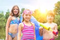 Portrait of smiling friends in swimwear standing with pool raft and squirt gun at lakeshore