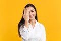 Portrait of smiling funny young woman in white casual shirt looking camera, covering face with hand isolated on yellow Royalty Free Stock Photo