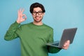 Portrait of smiling geek nerd young businessman in glasses show okay sign hold laptop isolated on blue color background