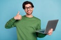 Portrait of smiling geek nerd young businessman in glasses show thumb-up hold laptop isolated on blue color background