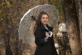 Portrait of smiling girl in black coat under transparent umbrella. Young woman against yellow trees in autumn park Royalty Free Stock Photo