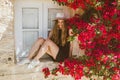 Portrait of smiling girl in black dress that sit on windows among purple bougainvillaea