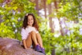 Portrait of smiling girl in forest sit on stone