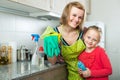 Little girl and mom tidy up at kitchen. Royalty Free Stock Photo