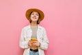 Portrait of smiling girl in light clothing and hat on pink background, holds smartphone and looks into camera with happy face. Royalty Free Stock Photo