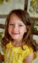 Portrait of a smiling girl in a yellow dress 6 years old. Pierced ear.Blue eyes, long hair.