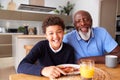 Portrait Of Smiling Grandfather Sitting In Kitchen With Grandson Eating Breakfast Before School Royalty Free Stock Photo