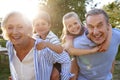 Portrait Of Smiling Grandparents Giving Grandchildren Piggyback Ride Outdoors In Summer Park