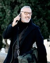 Portrait of smiling gray-haired man making call on his mobile phone while spending time in city park at sunny day Royalty Free Stock Photo