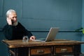 Portrait of smiling gray-haired mature older businessman talking on mobile phone sitting at table with laptop computer. Royalty Free Stock Photo