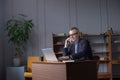 Portrait of smiling grey hair elderly man in glasses sitting by the table with laptop and talking on mobile phone Royalty Free Stock Photo