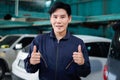 Portrait of smiling handsome Asian mechanic man in uniform giving thumbs up during work with vehicle, auto mechanic technician Royalty Free Stock Photo