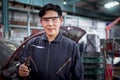 Portrait of smiling handsome Asian mechanic man in uniform welding car body panel vehicle, auto mechanic technician fixing,