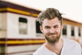 Portrait of smiling handsome European man standing at public train station. Happy backpack traveler or holiday vacation tourism