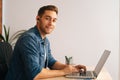 Portrait of smiling handsome freelance programmer male in wireless earphone working on laptop computer sitting at desk Royalty Free Stock Photo