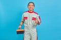 Portrait of smiling handsome man wearing mechanic uniform holding tool box and thumb up gesture isolated on blue background Royalty Free Stock Photo