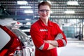 Portrait of smiling handsome mechanic in red uniform standing arms crossed with row of vehicle at car service shop, auto mechanic Royalty Free Stock Photo