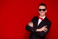 Portrait of smiling handsome stylish man in elegant black suit and sunglasses on red background Royalty Free Stock Photo
