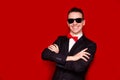 Portrait of smiling handsome stylish man in elegant black suit and sunglasses on red background. Business style Royalty Free Stock Photo