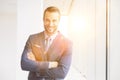 Portrait of smiling handsome young businessman standing with arms crossed in new office and yellow lens flare in background Royalty Free Stock Photo