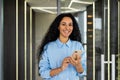 Portrait of a smiling happy businesswoman standing in the office holding a phone in her hands, a satisfied Indian worker Royalty Free Stock Photo