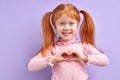 portrait smiling happy little girl making heart sign with hands isolated on purple background. Royalty Free Stock Photo