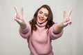 Portrait of a smiling happy woman showing victory sign and looking at camera isolated on the gray background Royalty Free Stock Photo