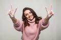 Portrait of a smiling happy woman showing victory sign and looking at camera isolated on the gray background Royalty Free Stock Photo