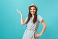 Portrait of smiling happy young elegant woman wearing dress, straw summer hat pointing hand aside on copy space isolated