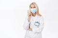 Portrait of smiling healthcare worker, lab employee in medical face mask, points finger up, shows advertisement, stands Royalty Free Stock Photo