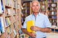 Portrait of smiling intelligent older man in library with book in hands