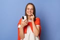 Portrait of smiling joyful cheerful woman wearing casual style clothing standing  over blue background, using cell phone Royalty Free Stock Photo